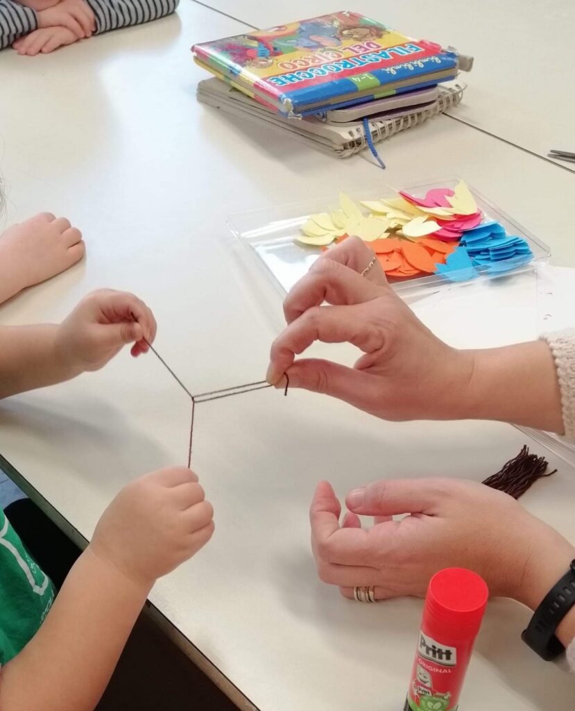 Immagine delle mani di una maestra e un bambino che stanno preparando del filo di lana nero da attaccare nel foglio per rappresentare un lavoretto inerente alla giornata della memoria  